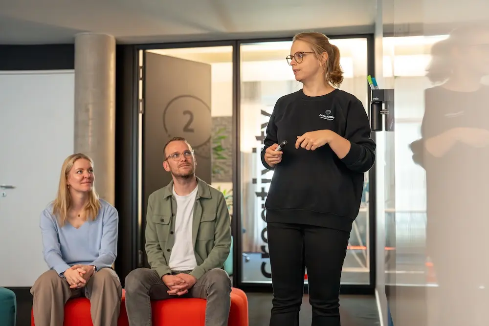 Anne Kritter am Whiteboard stehend vor zwei Teilnehmern beim Workshop zum Thema Burnoutprävention