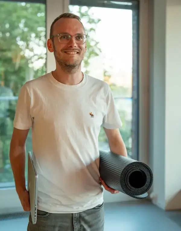 Smiling participant holding a yoga mat and a laptop - symbolising physical and mental resilience training